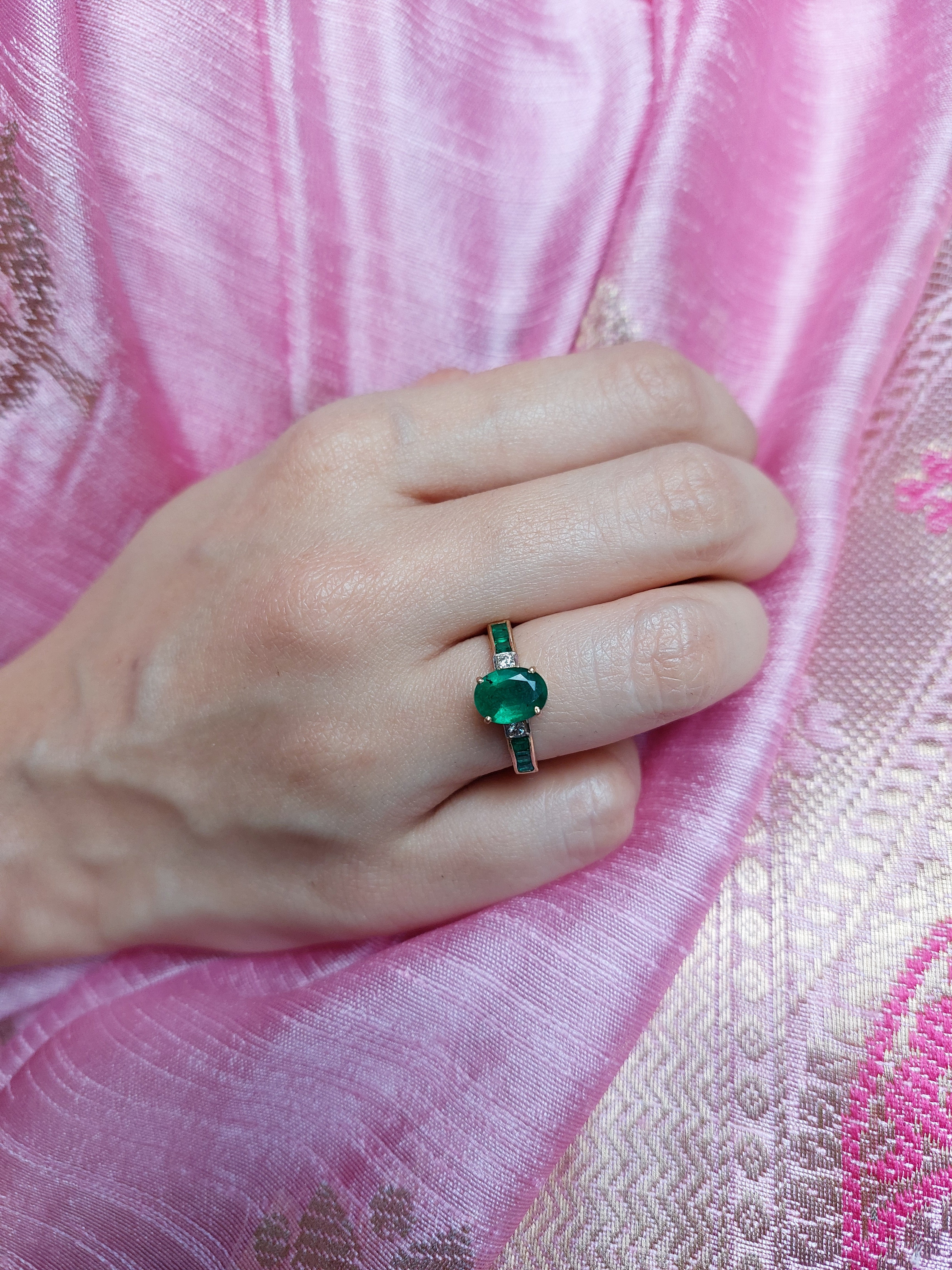 14K gold emerald ring on hand against pink textured fabric