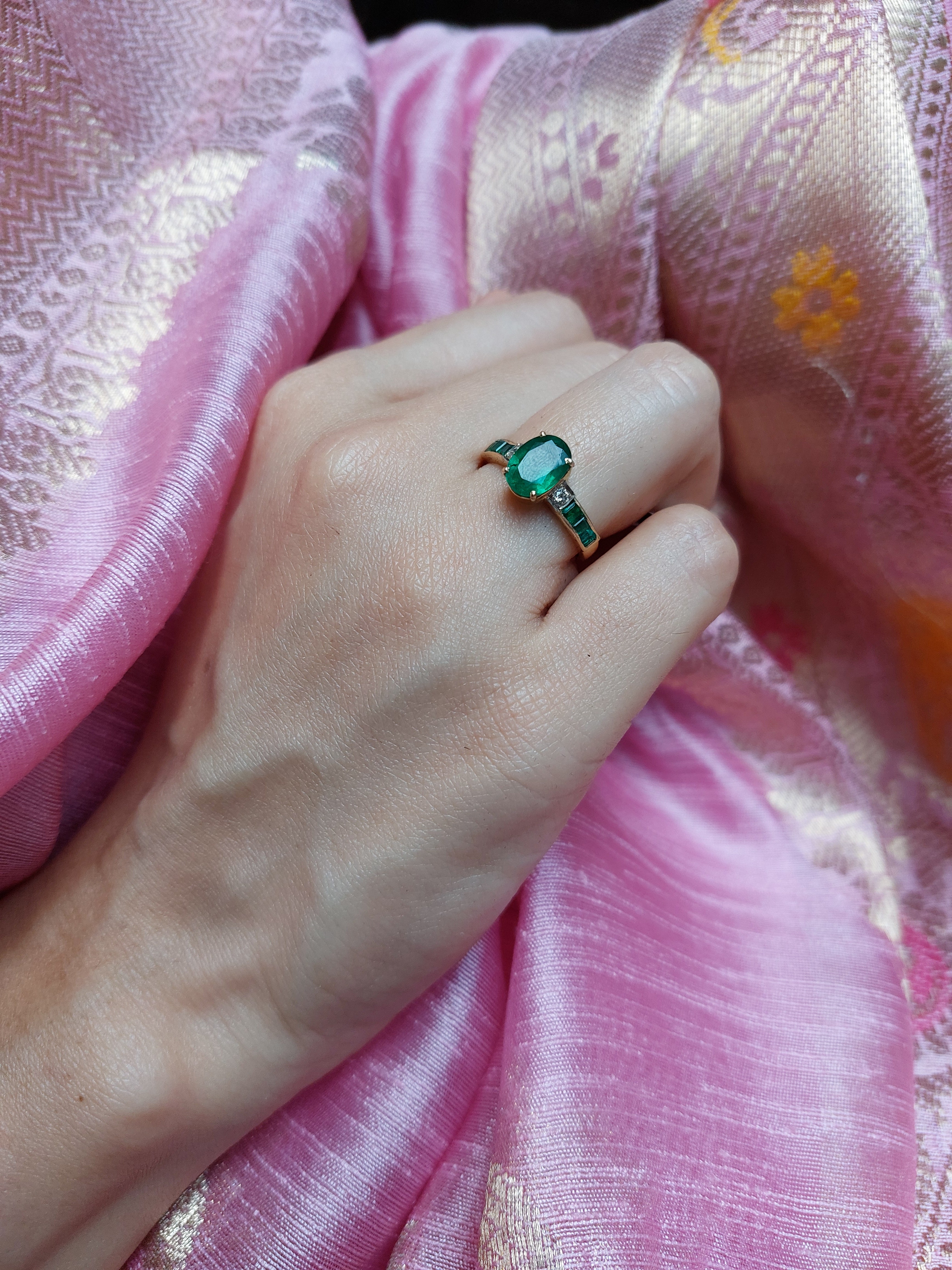 14K gold emerald ring on hand over pink silk fabric