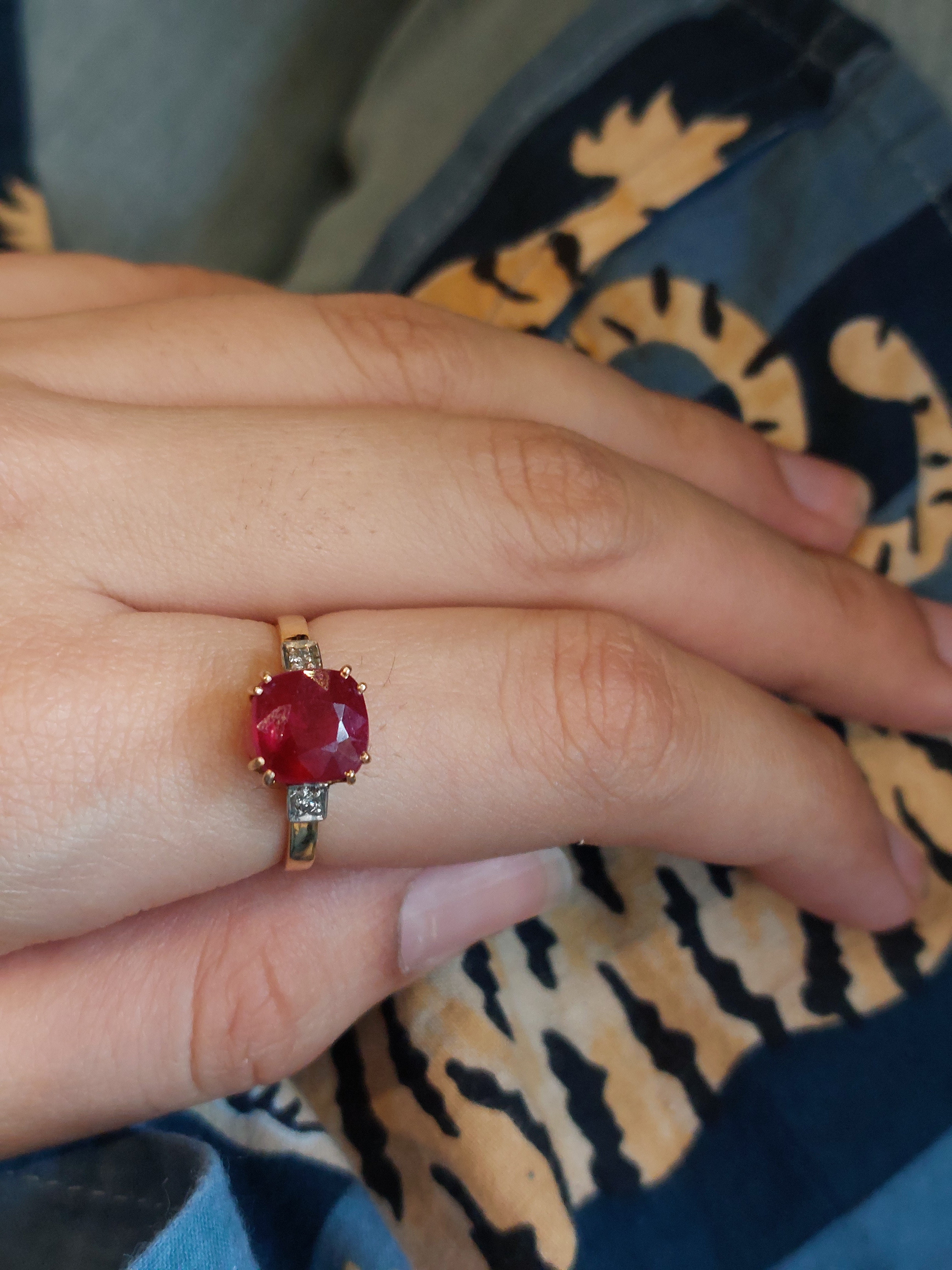 Gold ring with a large oval red gemstone and small clear accent stones on a hand.