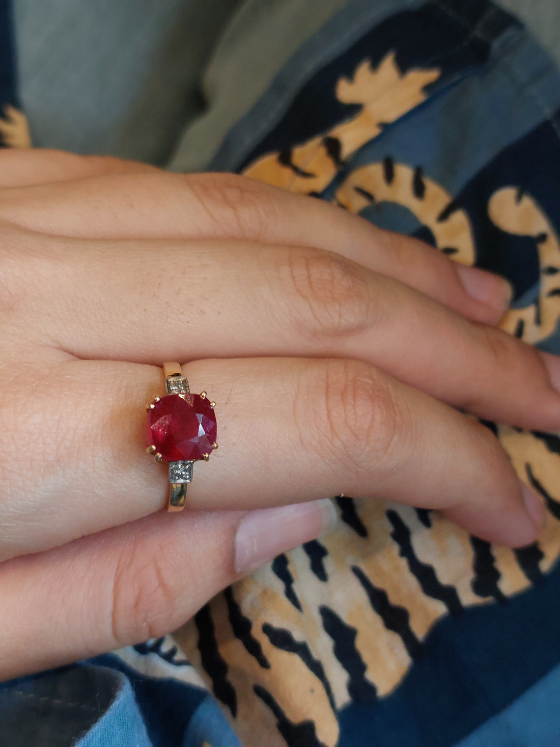 Gold ring with a large oval red gemstone and small clear accent stones on a hand.