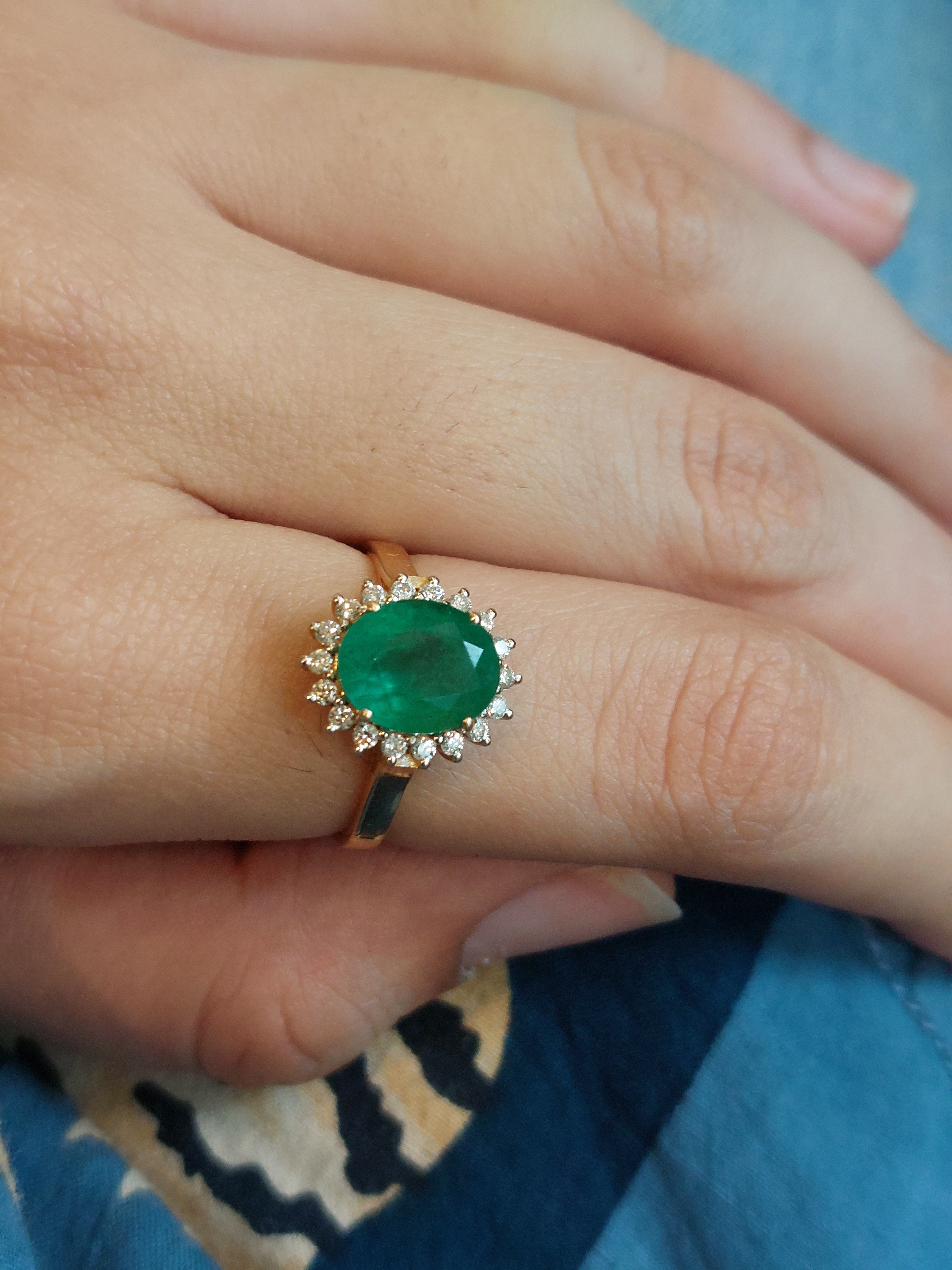 14K gold oval emerald ring with diamond accents on finger