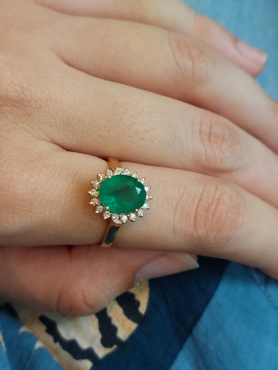 14K gold oval emerald ring with diamond accents on finger