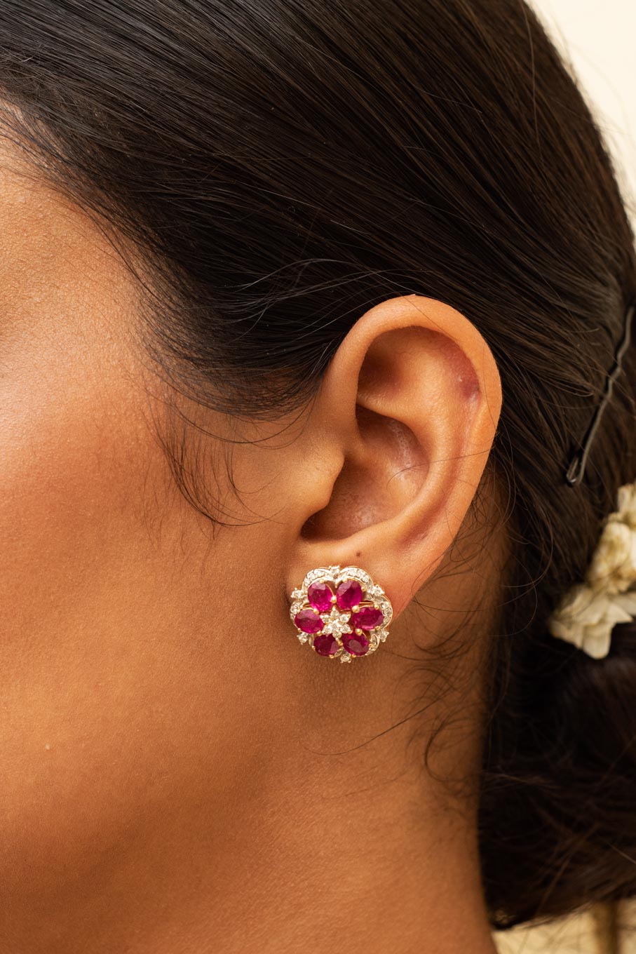 Gold floral earrings with ruby petals and diamond accents worn on ear.