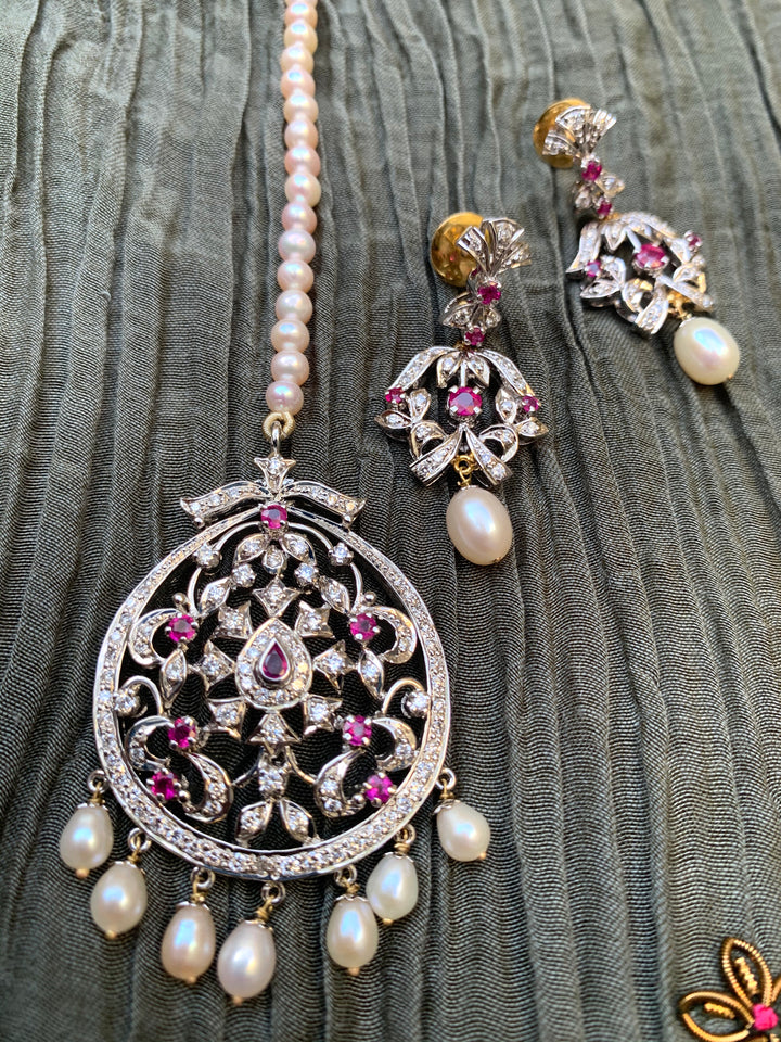 Silver Manik diamond tika with pink stones and hanging pearl drops, paired with matching earrings.