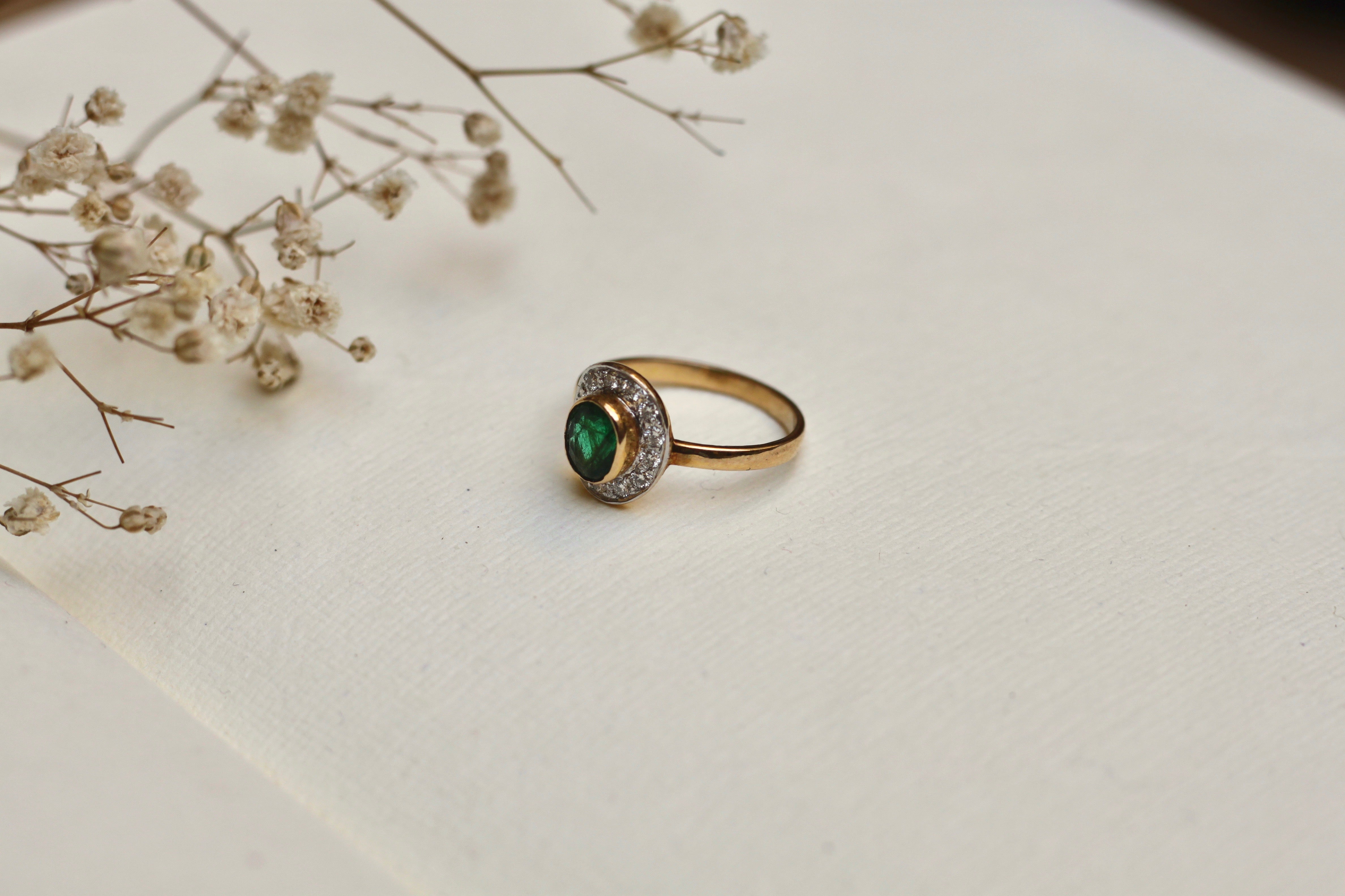 14K gold emerald ring with diamond halo on beige background