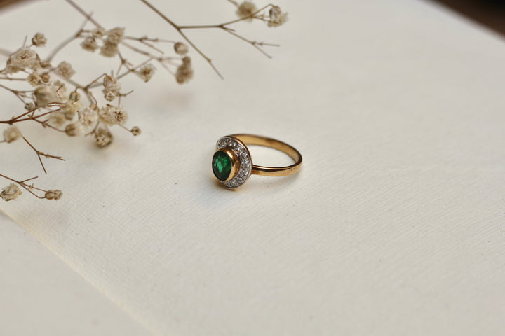 14K gold emerald ring with diamond halo on beige background