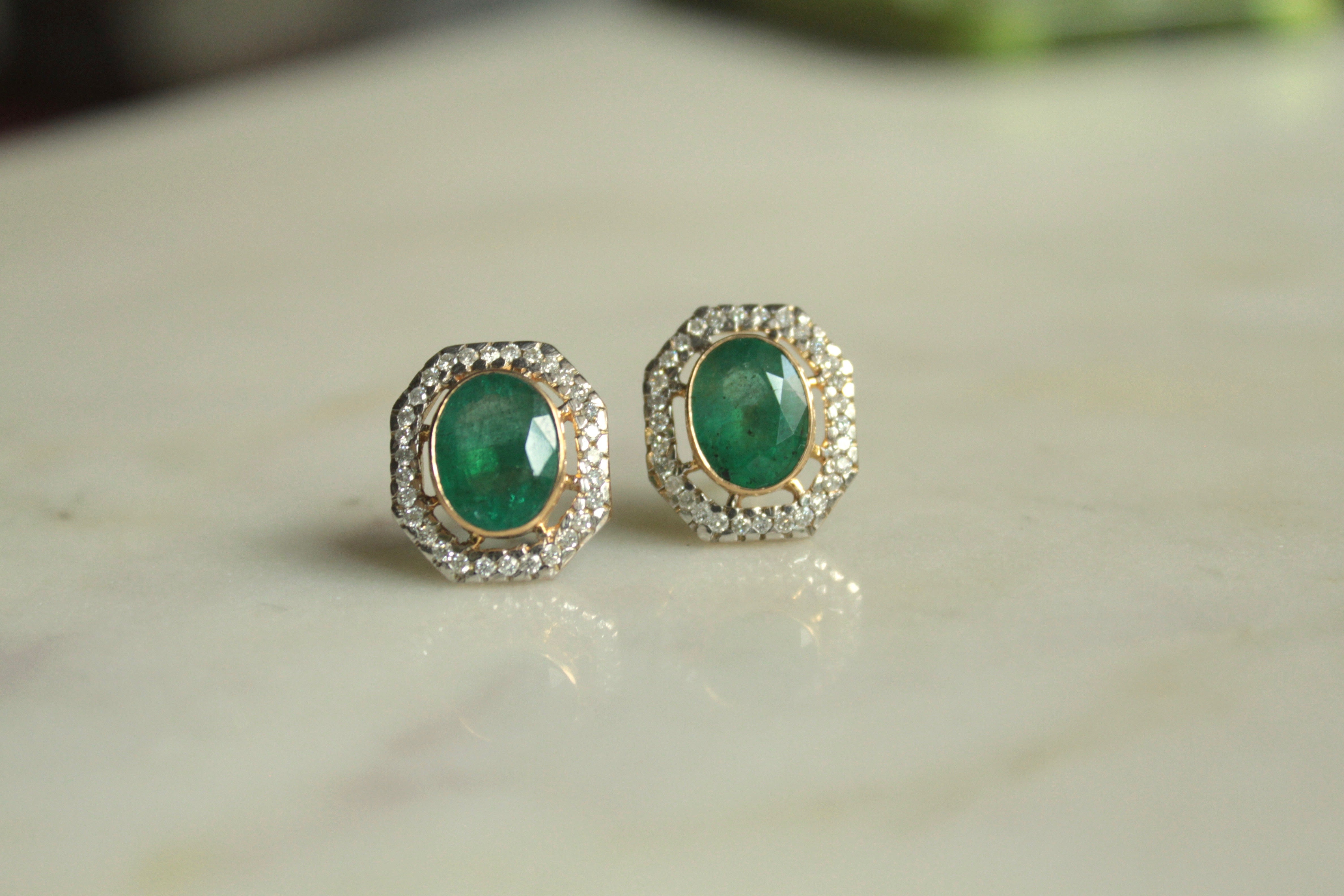 14K gold oval emerald earrings on marble surface