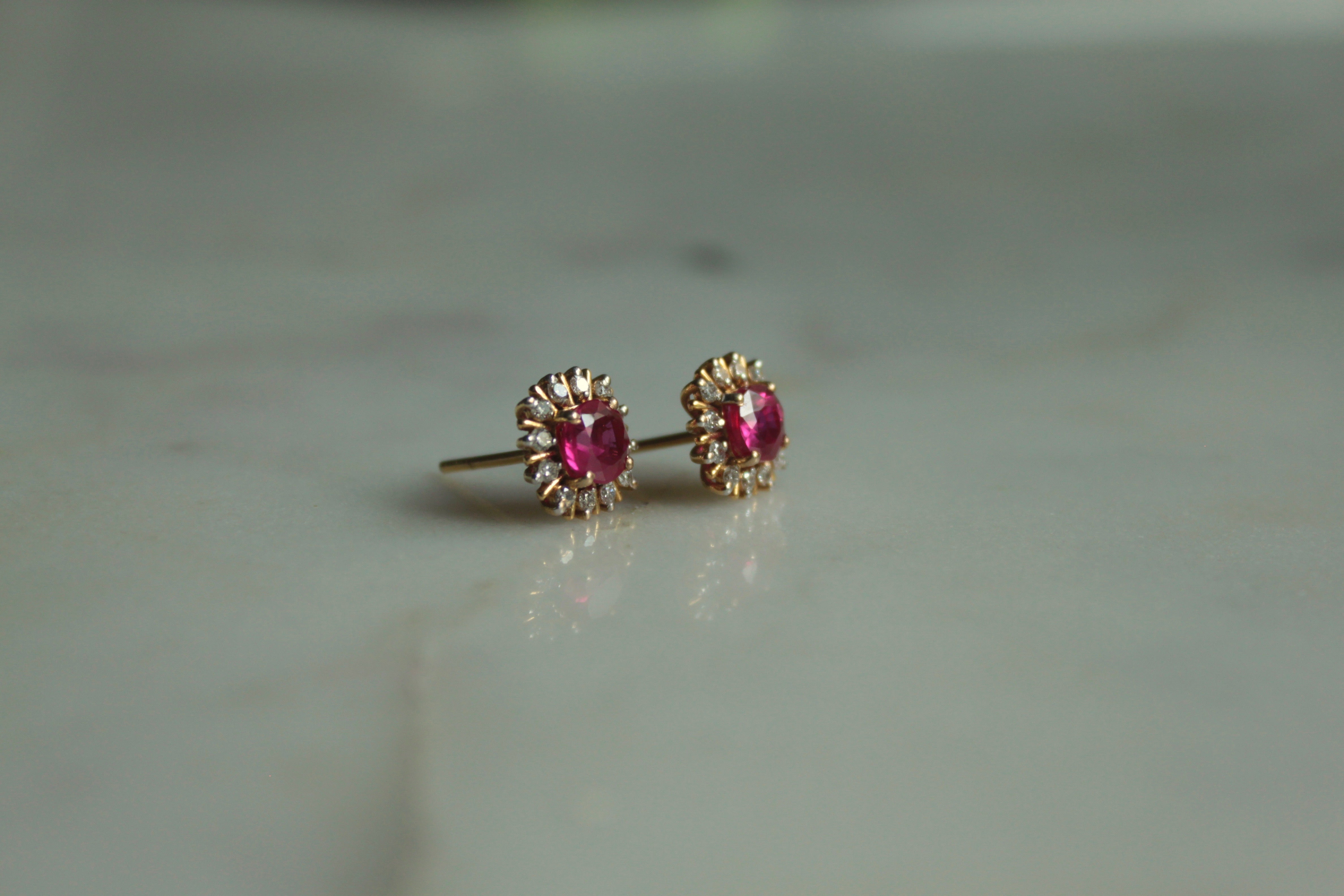 14K gold oval ruby stud earrings on marble surface