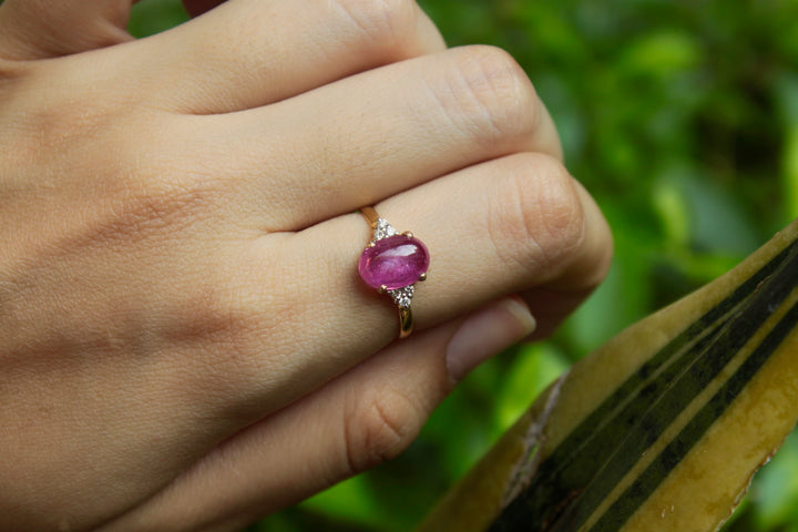 14K gold ruby ring worn on finger against green background